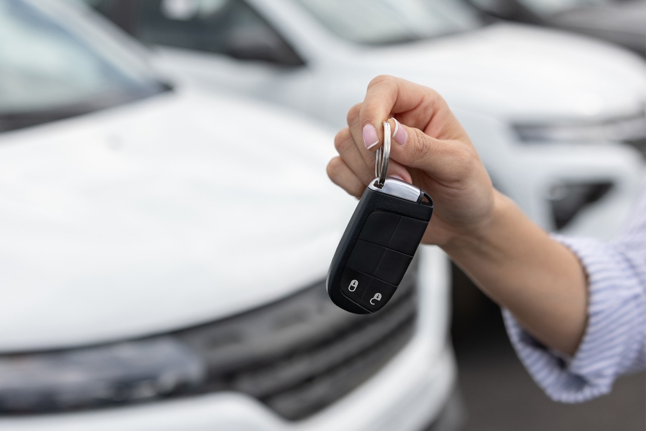 Close-up on a woman holding the keys of a car at the dealership - car ownership concepts