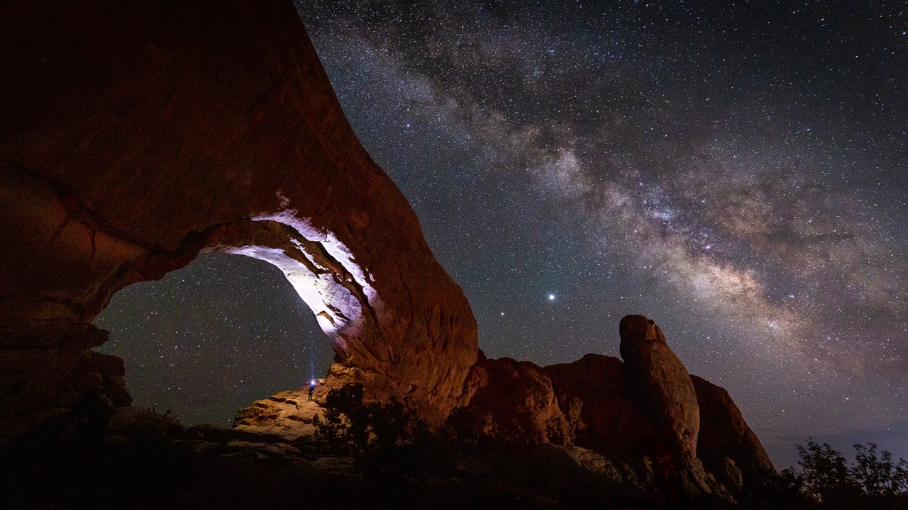 The Milky Way stretches across the dark night sky in Arches National Park.