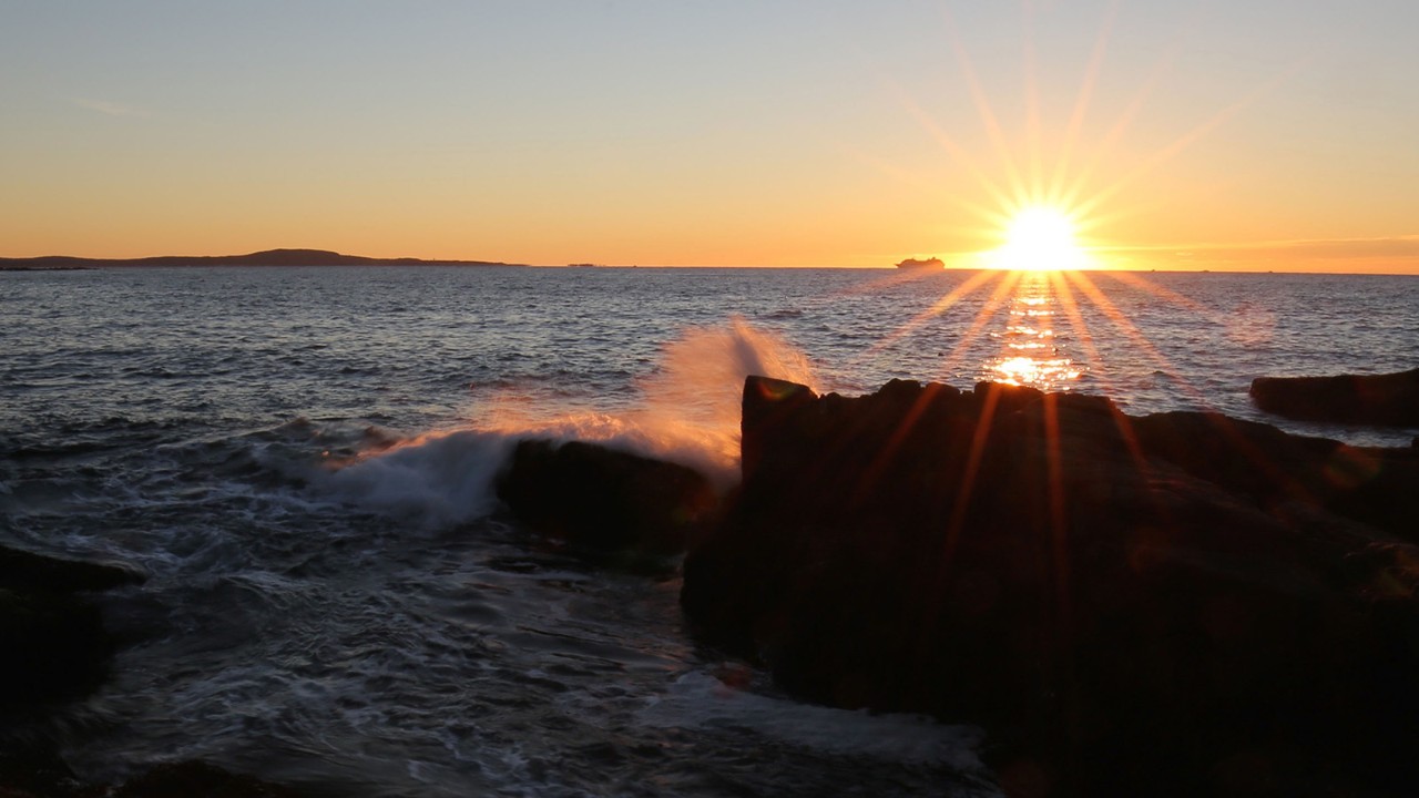 The sun rises as waves crash into the coastline.